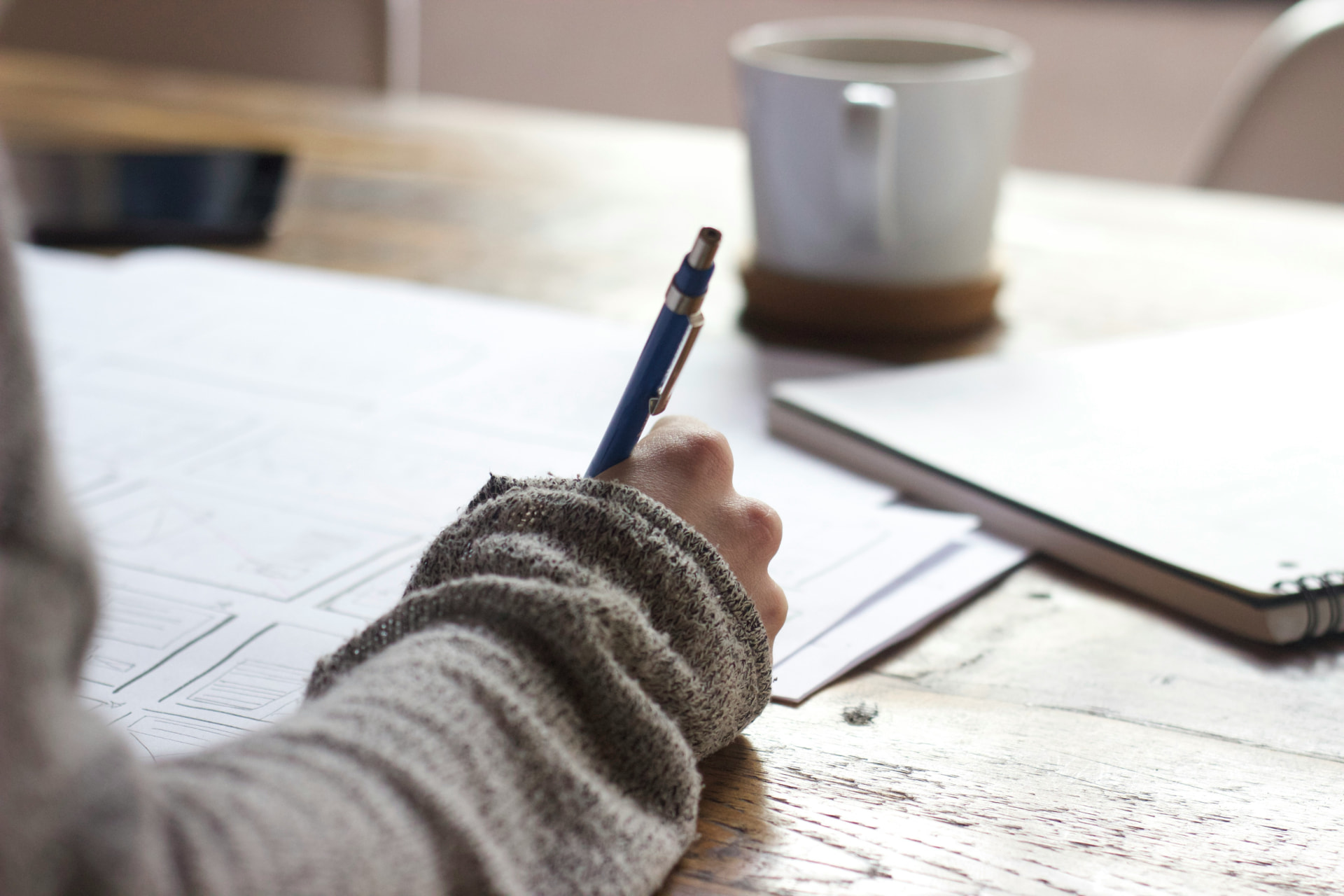 A student writing notes at a desk beside a cup of coffee